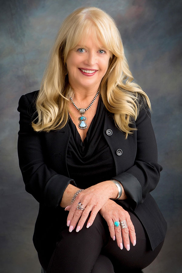 Photo of Attorney Nancy Cronin- blonde woman in black suit with turquoise and silver jewelry